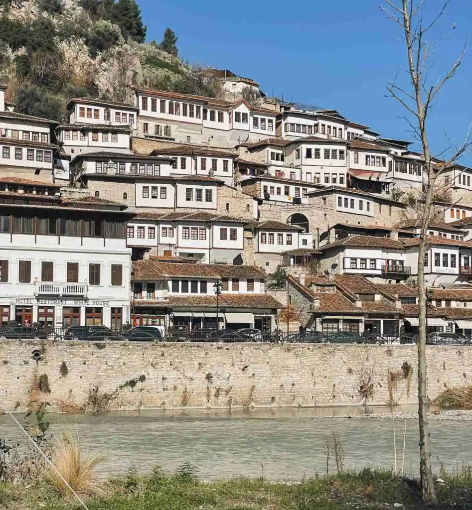 A scenic view of Berat Old Town in Albania, showcasing its signature white Ottoman-era houses stacked on the hillside, with red-tiled roofs and stone walls, under a bright sky.