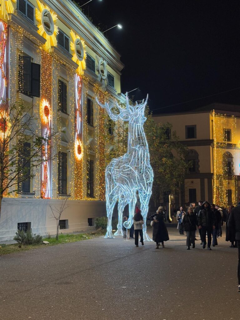 Tirana city center at night during the Christmas market with festive lights, decorated stalls, and crowds walking through the square. Visiting seasonal events like this is one of the most vibrant things to do in Tirana as locals and visitors gather to enjoy the lively atmosphere.
