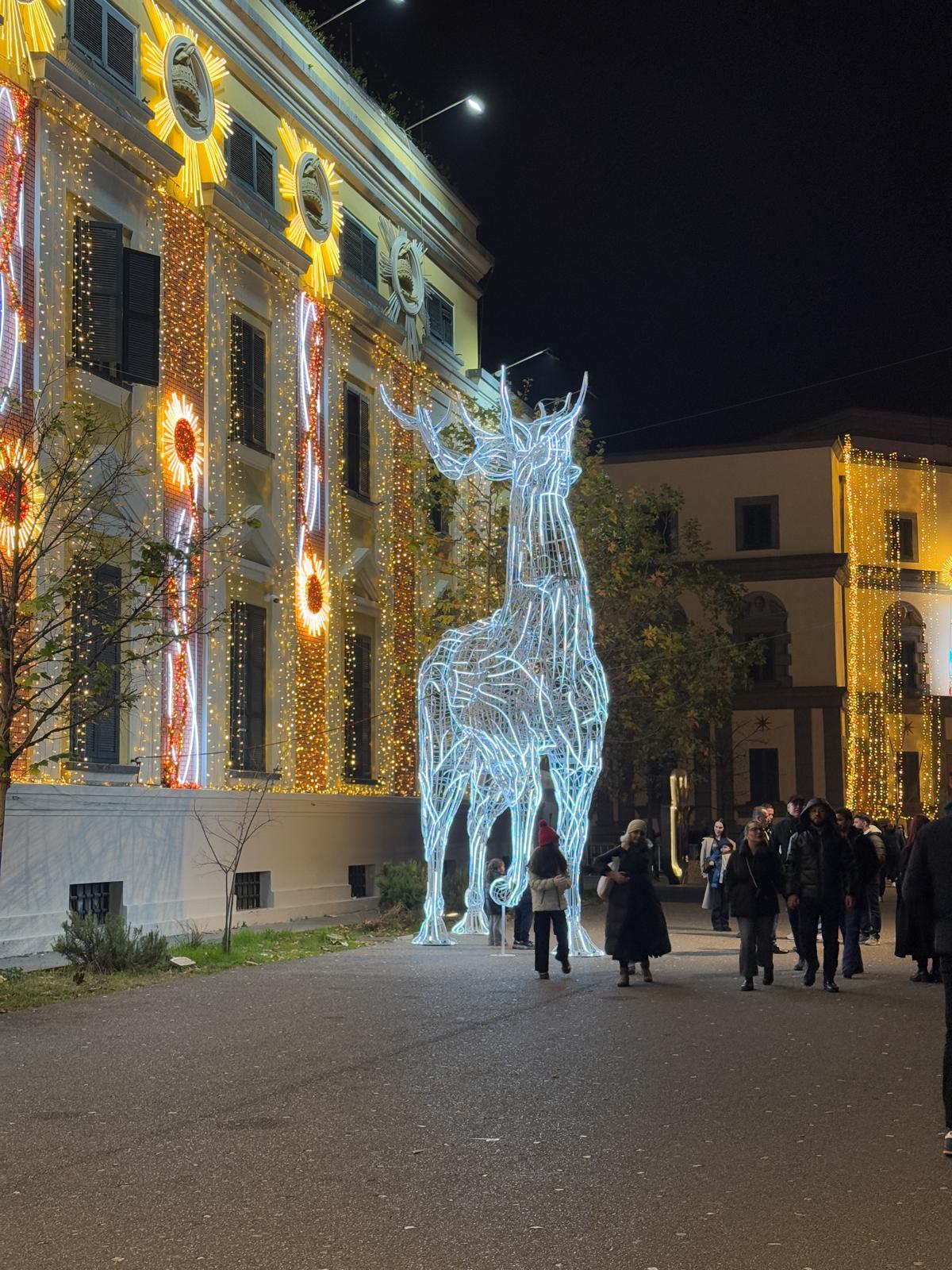 Tirana city streets at night decorated with bright Christmas lights and festive ornaments illuminating buildings and trees. The lively winter atmosphere reflects a cheerful holiday version of Tirana nightlife with glowing decorations and people enjoying the seasonal city center ambiance.