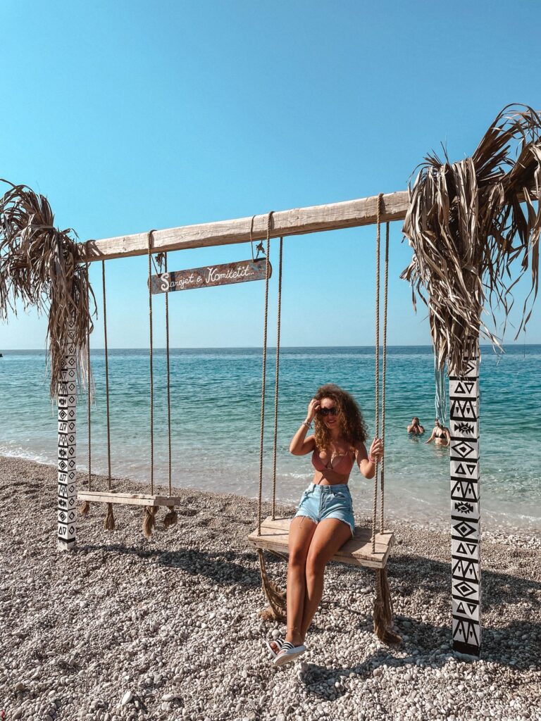 Woman standing on Dhermi Beach with vivid blue water and rugged mountains in the background, highlighting the dramatic scenery explored in one week to the Albanian Riviera.
