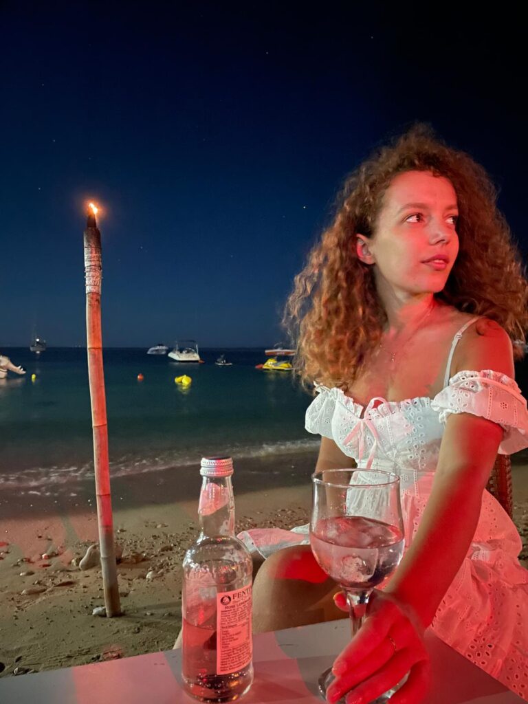 A person holding a drink at a seaside bar in Himara with tables and the coastline in the background. This image reflects everyday spending in Albania and whether you need lek in Albania for bars and small venues