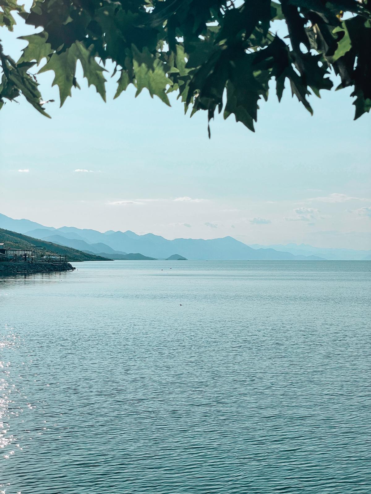 Shiroka Lake with calm water reflecting surrounding mountains and small lakeside houses. A peaceful stop near the Albania Montenegro border crossing route.