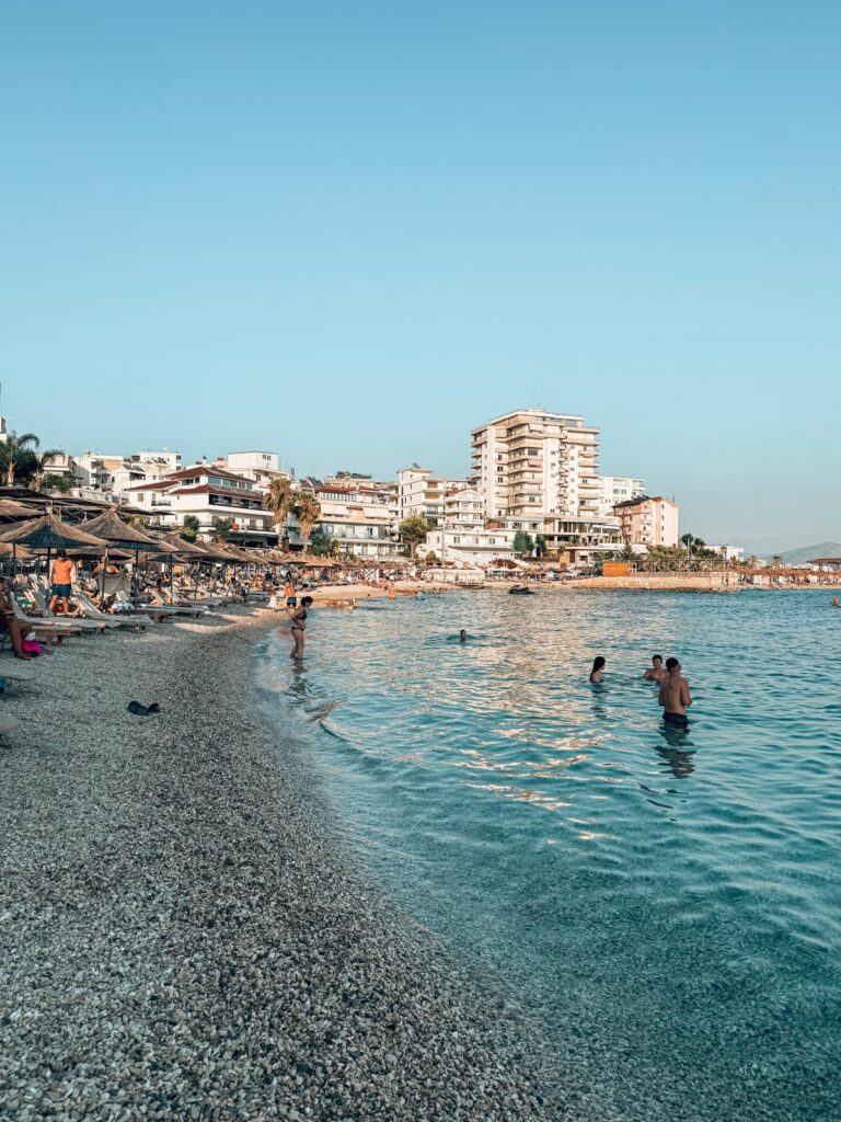 Saranda Beach with turquoise water and seaside promenade lined with buildings and umbrellas, a lively shoreline just minutes from the corfu to saranda ferry port.