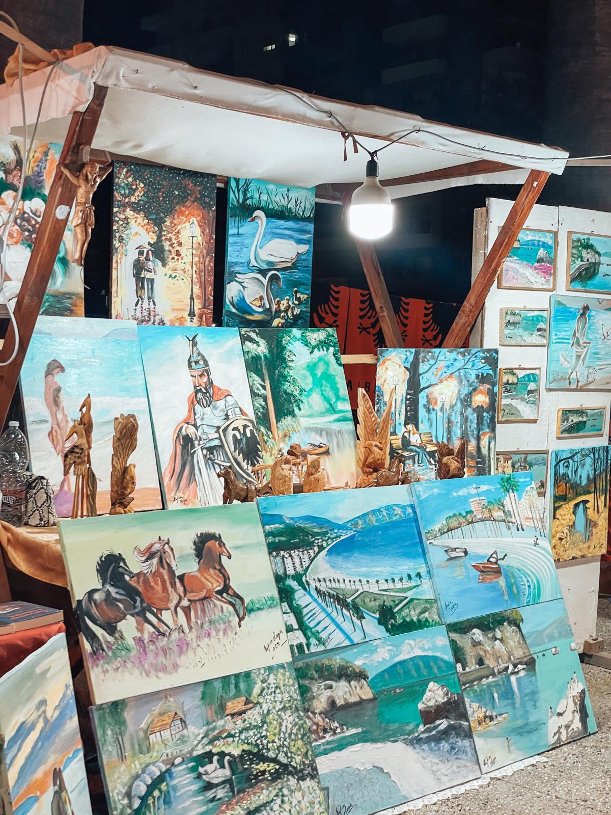 Night market stand in Vlora lit by warm lights with vendors selling snacks and local goods. A lively evening scene for travelers wondering where to go in Albania.