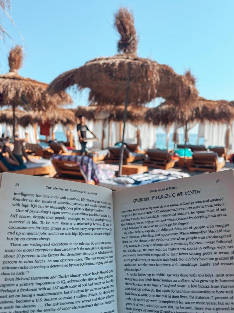 Girl reading a book while sitting on a sandy beach with gentle waves nearby, capturing a quiet coastal moment along the Albanian Riviera after the corfu to saranda ferry trip.