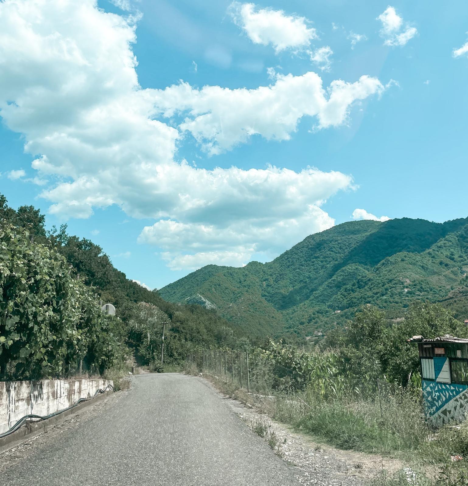 Winding paved road cutting through the rugged Albanian Alps with steep rocky mountains rising on both sides. The quiet mountain landscape highlights how remote travel experiences are part of why people ask if Albania is a cheap country to visit.
