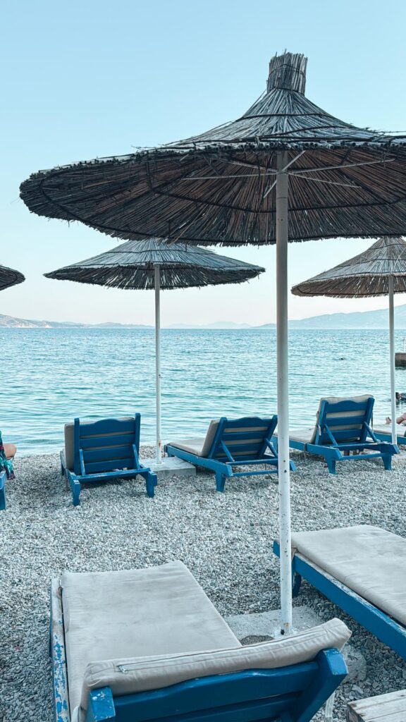 Saranda Beach with clear turquoise water and a lively promenade lined with seaside buildings. A popular southern stop for travelers making their way from Albania to Greece.