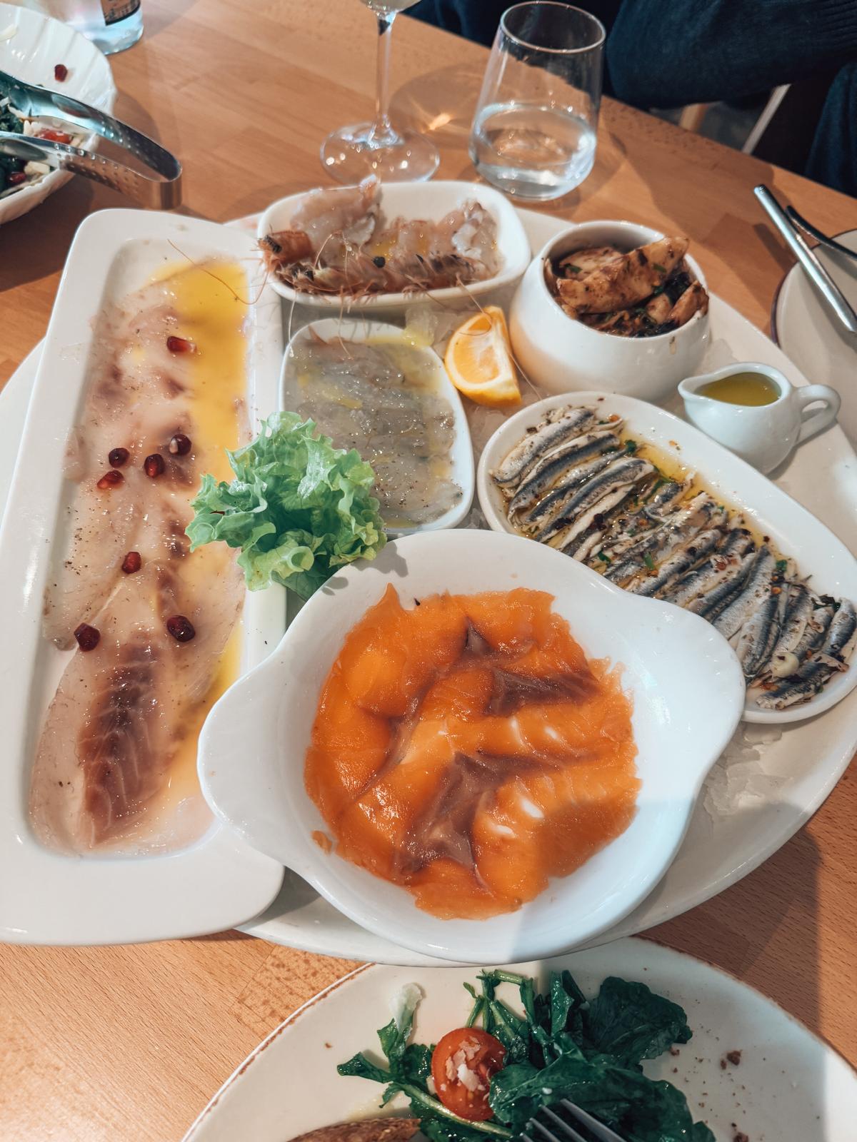 Indoor lunch table in Tirana with plates of Albanian food and drinks set on a café table along a lively city street. Relaxed dining scene during one of the popular weekend getaways in Albania.