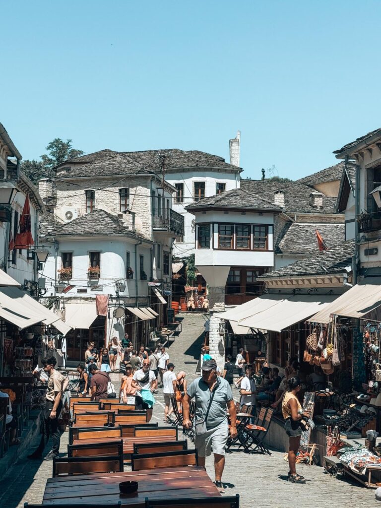 Narrow cobblestone street of Gjirokastra Bazaar in Albania lined with traditional stone buildings, colorful market stalls, and local crafts under soft daylight. This historic market street is a charming and Instagrammable spot in Albania.