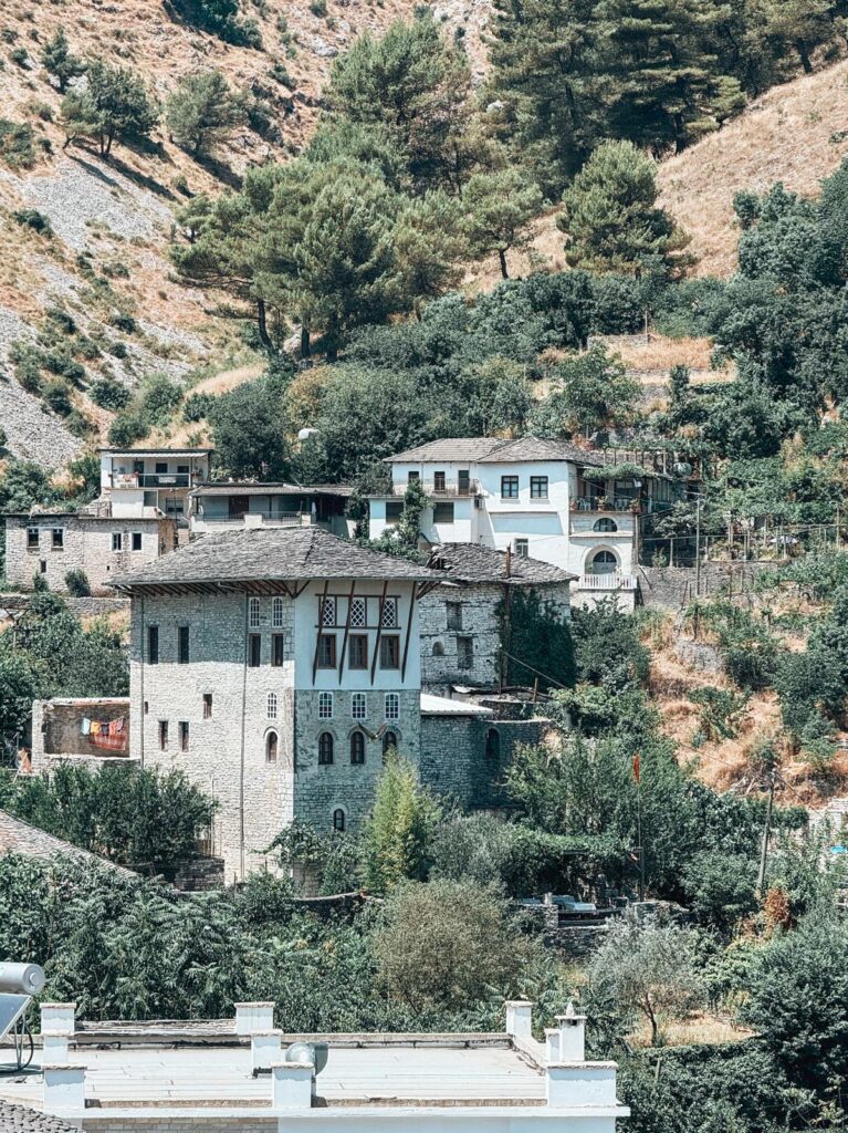 Stone Ottoman-era houses with terracotta roofs cascading down the hillside in Gjirokastra Old Town. Iconic historic stop often included on an Albania road trip through southern Albania.