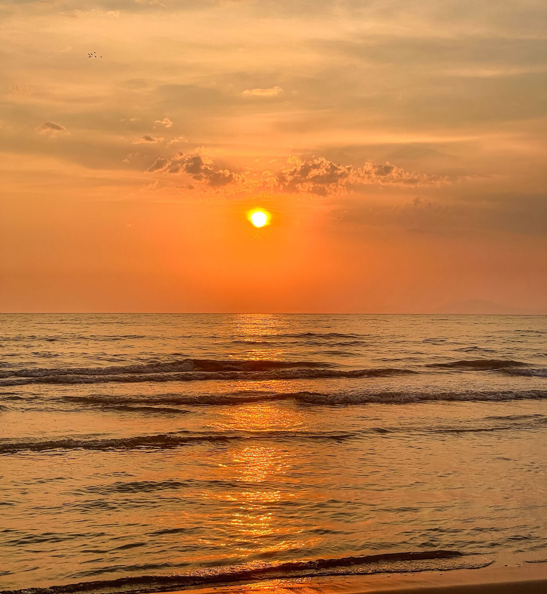 Sunset over Shëngjin Beach with warm orange and pink hues reflecting on the calm sea as the shoreline stretches into the distance. The peaceful coastal view captures a relaxing evening during backpacking Albania.