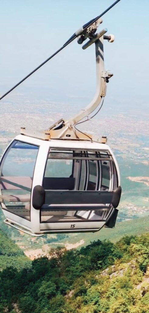 Cable car cabins glide above dense green forest on the way up Mount Dajti, offering panoramic views of the landscape on a popular escape for day trips from Tirana.
