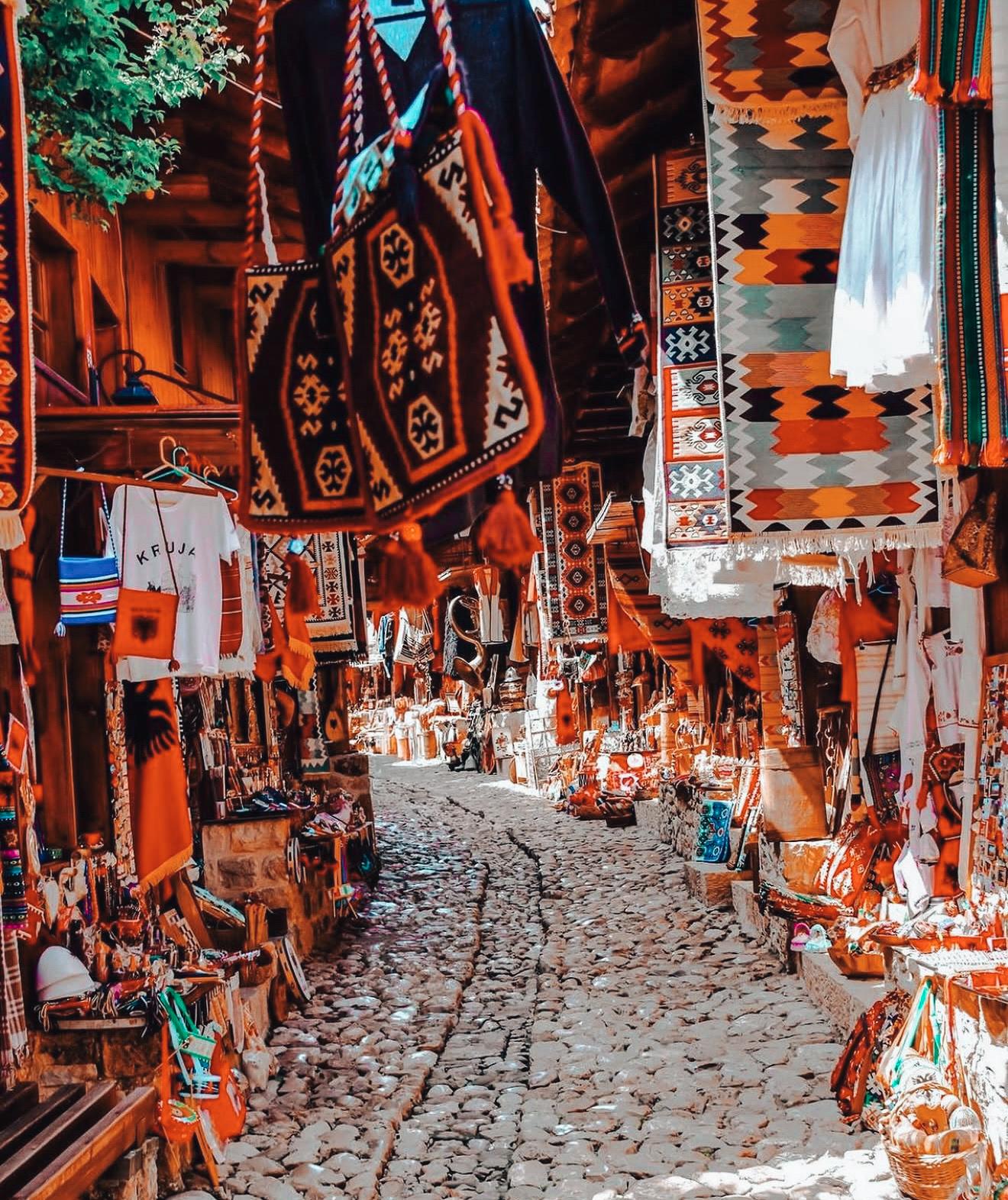 Traditional wooden stalls line Kruja Bazaar with handmade rugs, antiques, and souvenirs on display, capturing a historic shopping street often visited on day trips from Tirana.