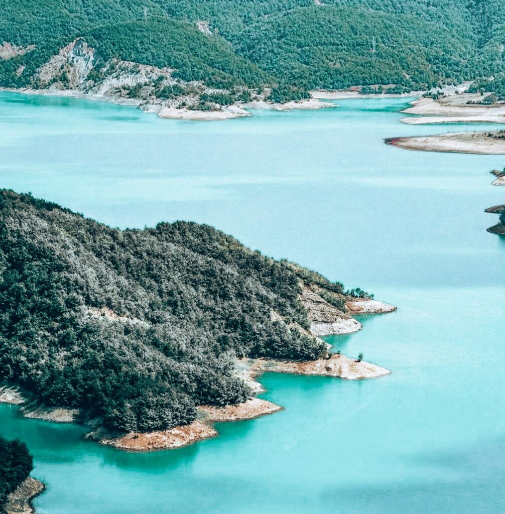 Quiet lakeside view of Lake Bovilla with still water reflecting the surrounding cliffs and soft natural light.