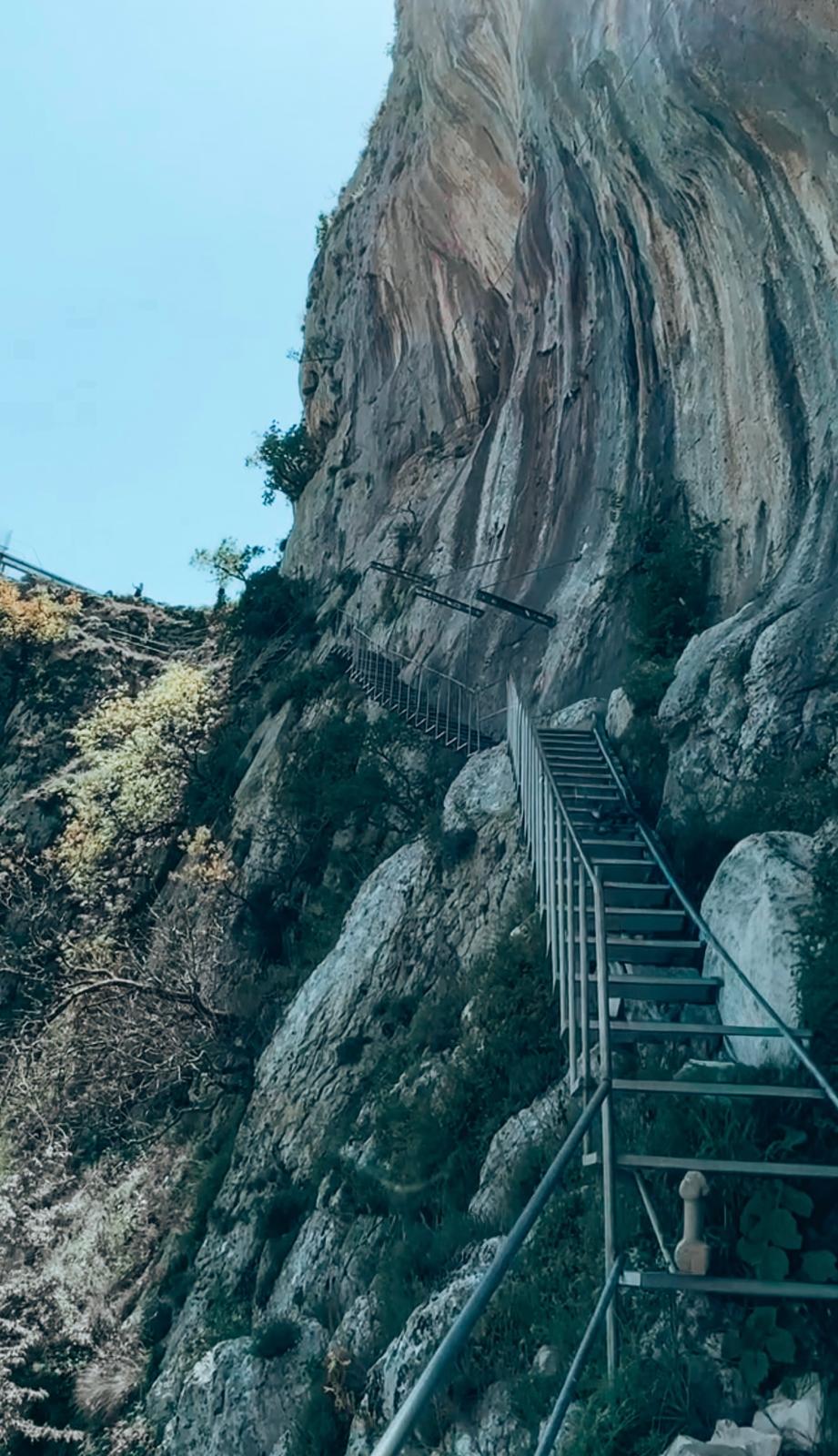 Steep stone stairs carved into the hillside leading up to a scenic viewpoint overlooking Lake Bovilla surrounded by rugged mountains.