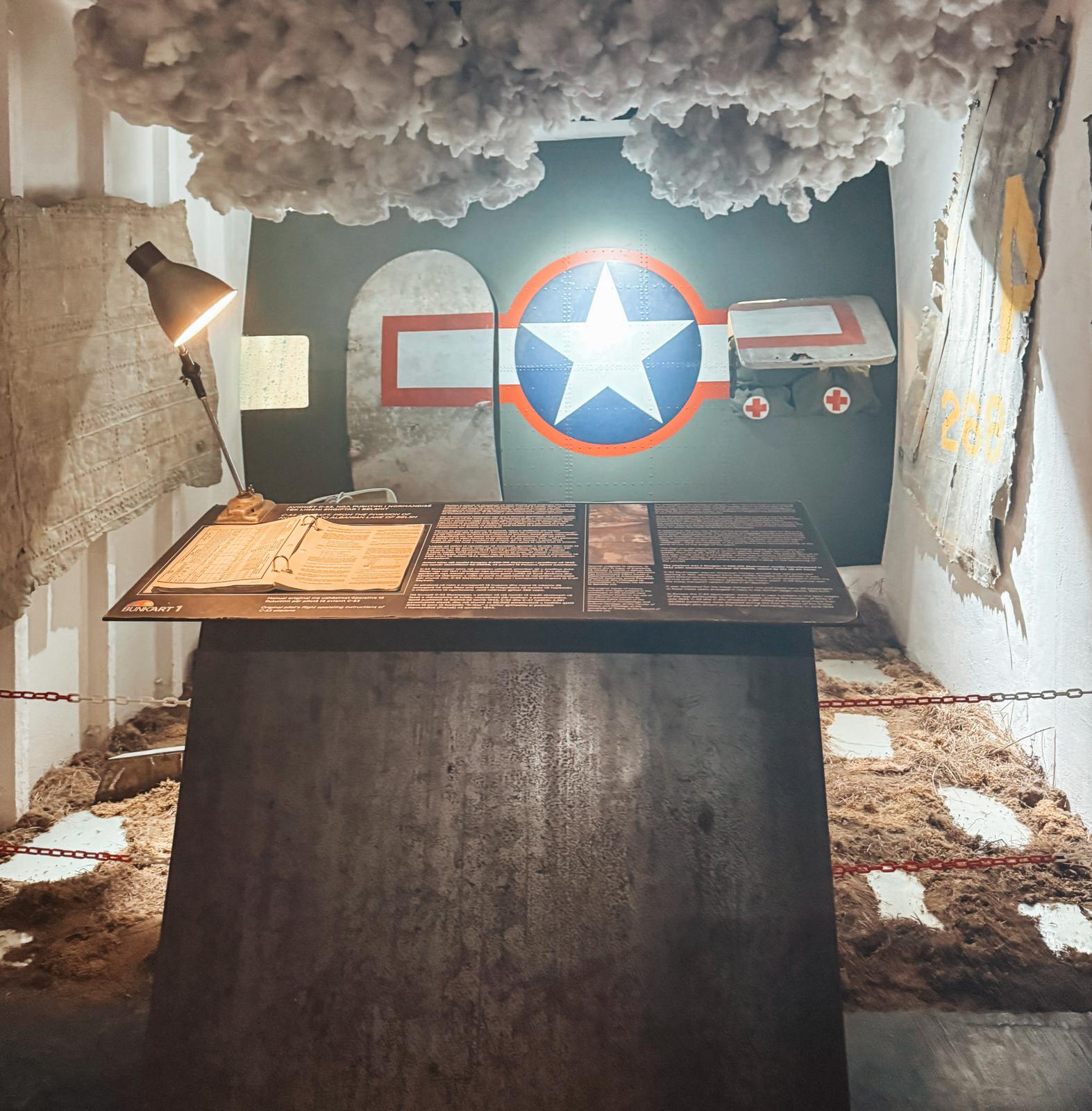 Alt text: A simple working table with a desk lamp casting soft light over a worn surface, suggesting a modest workspace from the communist era. The scene helps illustrate the conditions experienced when visiting a bunker in Albania and exploring its preserved interiors.