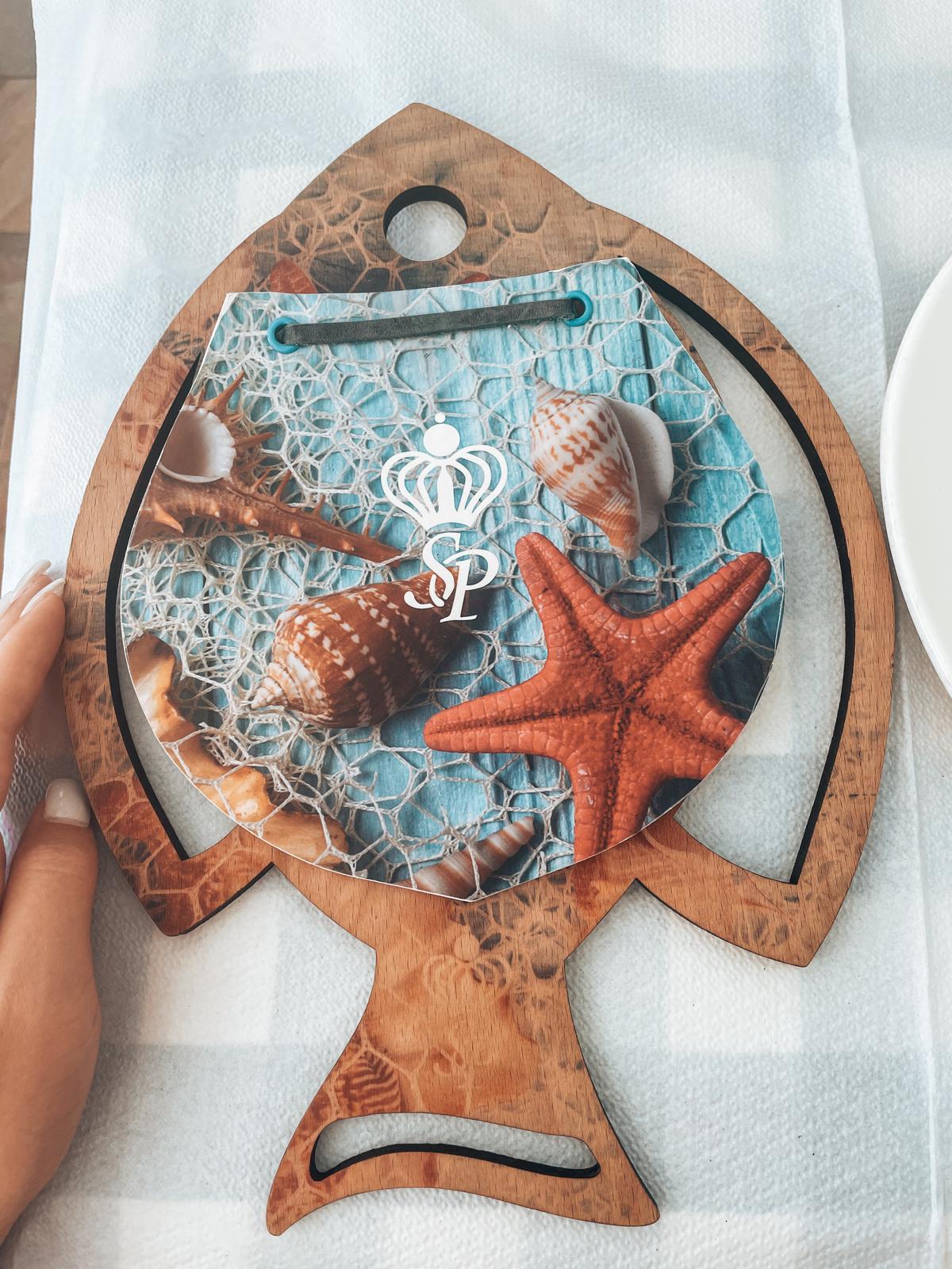 Beach inspired restaurant menu featuring a fish shaped design and seafood dishes, placed against a coastal themed backdrop on the Albanian Riviera.