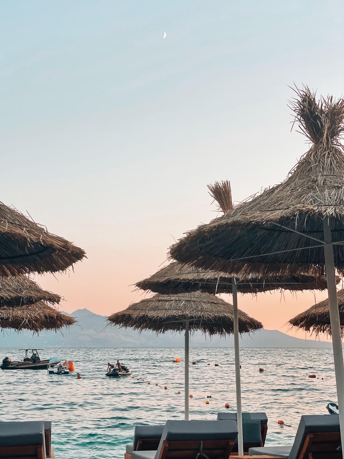 Sunset over the Himara Riviera in Albania with warm orange light reflecting across the Ionian Sea and rugged coastal hills fading into silhouette. The peaceful glow over the shoreline captures the scenic beauty that makes this area part of the best beaches in Albania.