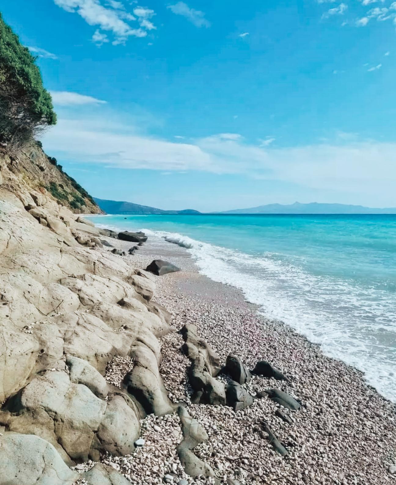 Gjipe Beach in Albania nestled between steep canyon cliffs with a narrow stretch of white pebbles leading to clear turquoise water in the Ionian Sea. The remote and dramatic landscape highlights why it is often listed among the best beaches in Albania.