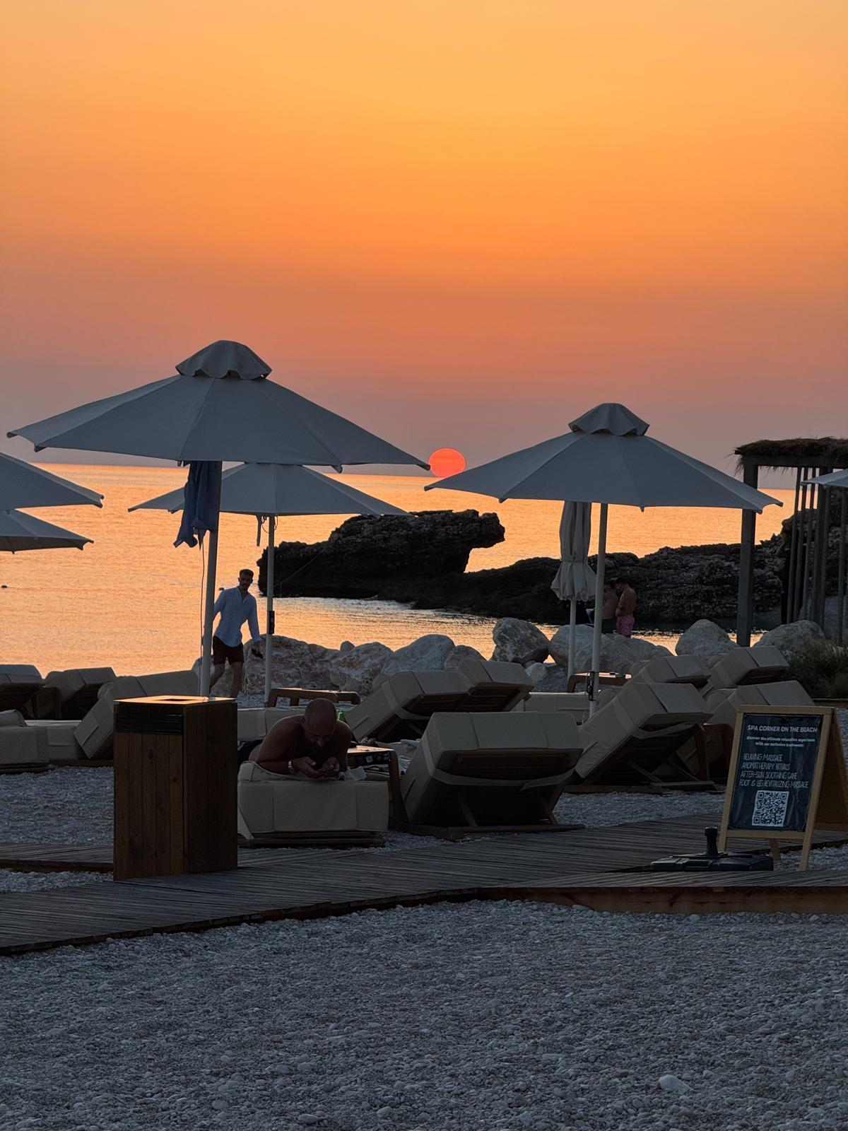 Alt text: Sunset over Palasa Beach in Albania with golden light reflecting across calm sea water and the shoreline glowing in warm orange and pink tones. The peaceful coastal view captures why Palasa is often included among the best beaches in Albania.