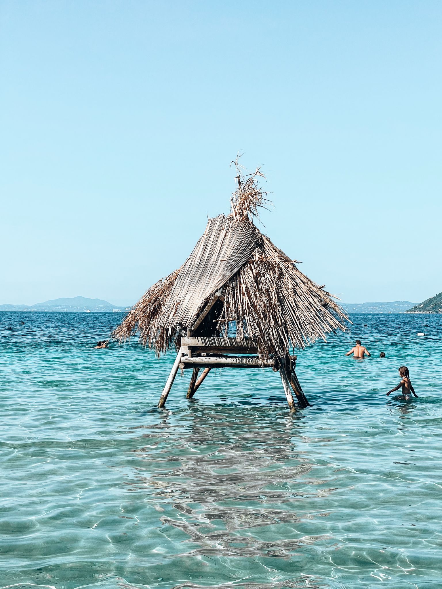 Dry tree branches stretching over the rocky shoreline at Pema e Thatë in Albania with clear turquoise water in the background. The quiet coastal landscape reflects the untouched scenery often found around secret beaches in Albania.