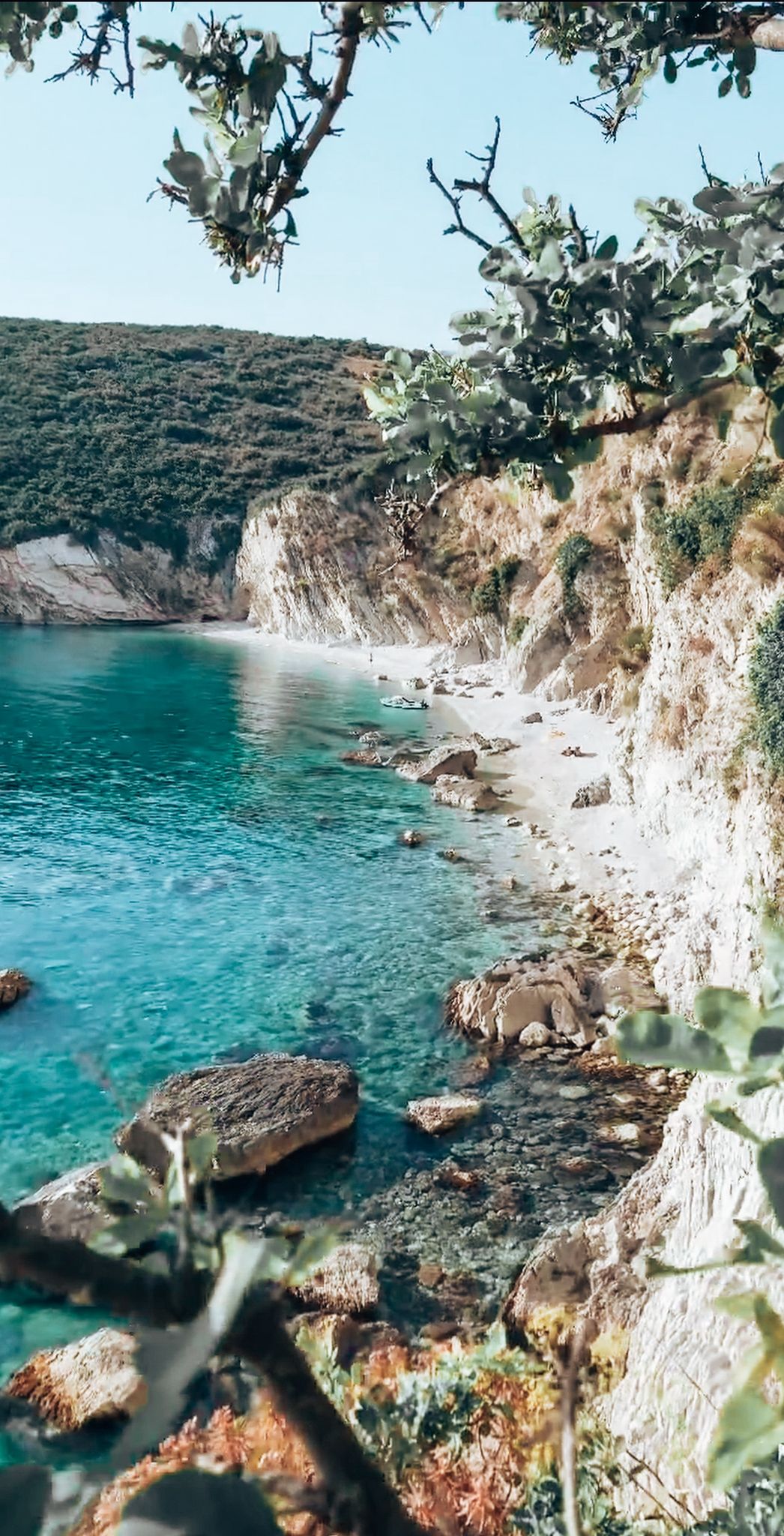 Secluded cove at Gjiri i Filikurit with crystal clear turquoise water surrounded by steep rocky cliffs and greenery. The hidden bay captures the wild and untouched feel of secret beaches in Albania.