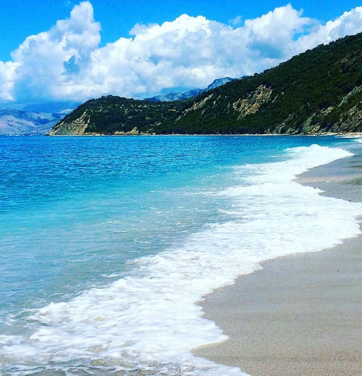 Panoramic view of the Lukovë coastline with deep blue Ionian Sea water, green hills, and scattered seaside homes along the shore. The peaceful setting showcases the natural beauty and hidden charm of secret beaches in Albania.