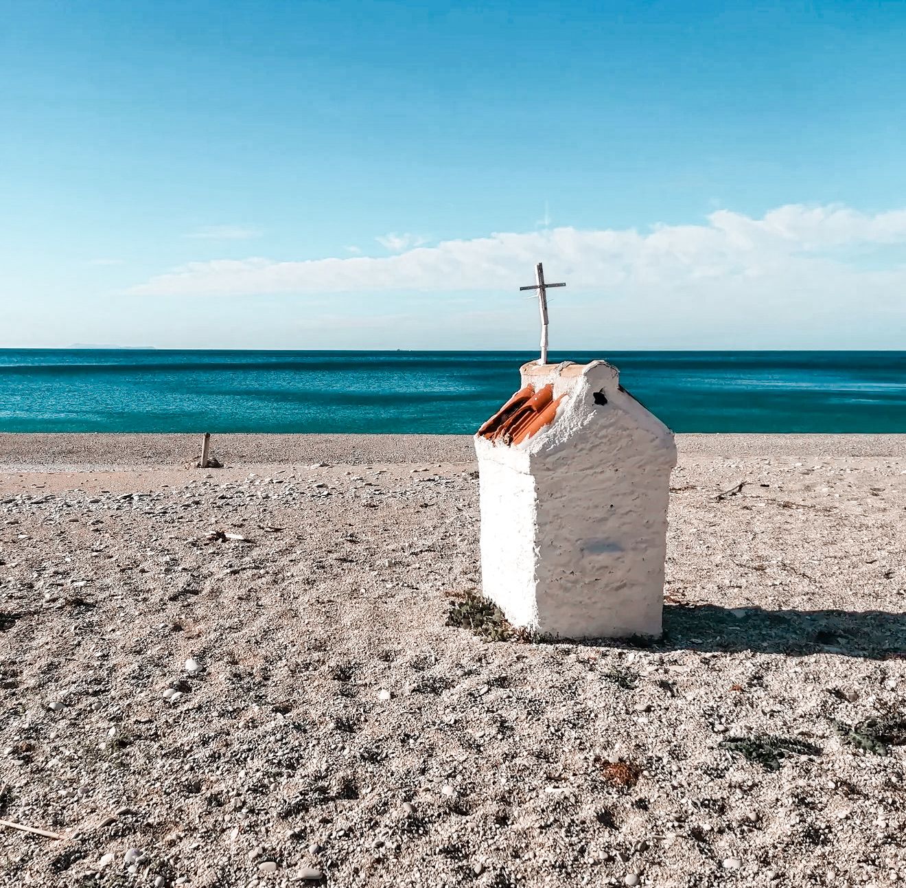 Small white church statue overlooking the turquoise water at Gjiri i Filikurit in Albania. Rocky cliffs and the secluded beach below highlight the hidden coastal beauty often associated with secret beaches in Albania.