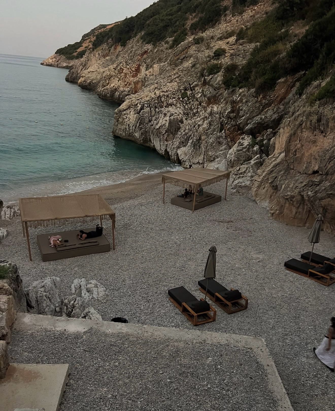 View of the turquoise sea from Folie Marine Beach Bar with sun loungers, umbrellas, and the Albanian coastline stretching into the distance. The relaxed seaside setting highlights the scenic atmosphere of beach bars and clubs in Albania.