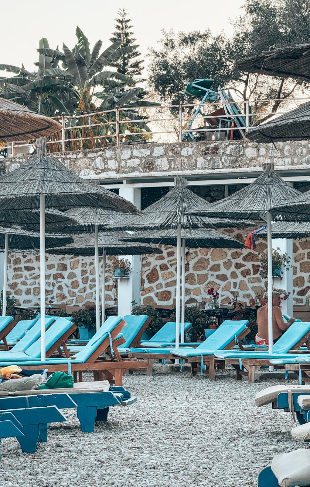 Beachgoers enjoying the clear blue water and pebbled shoreline of Saranda. The coastal setting is representative of the beaches highlighted throughout the guide.