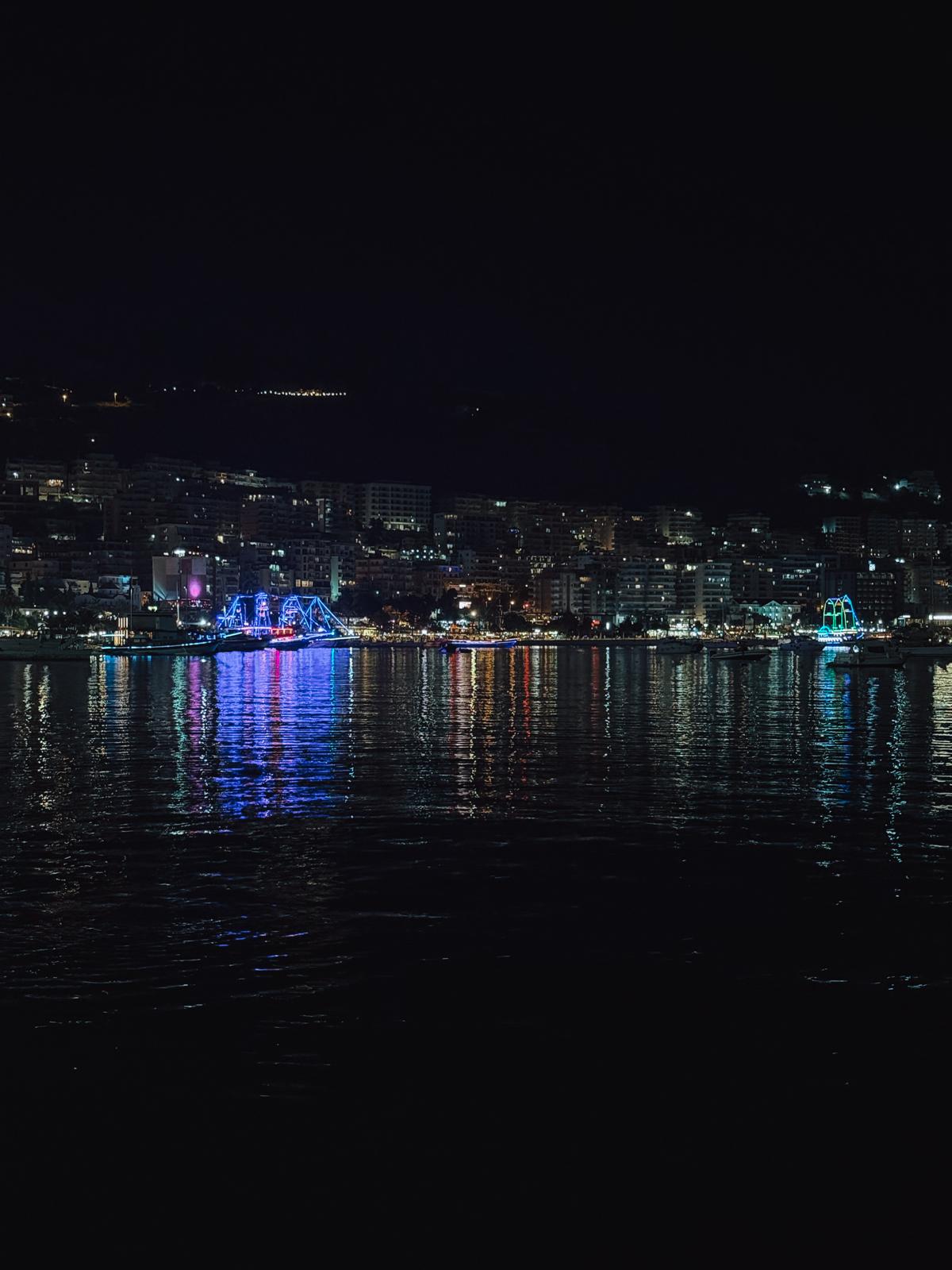 Saranda waterfront illuminated after sunset with city lights reflecting on the sea. The evening atmosphere shows a different side of the coastal destination after the beaches quiet down.
