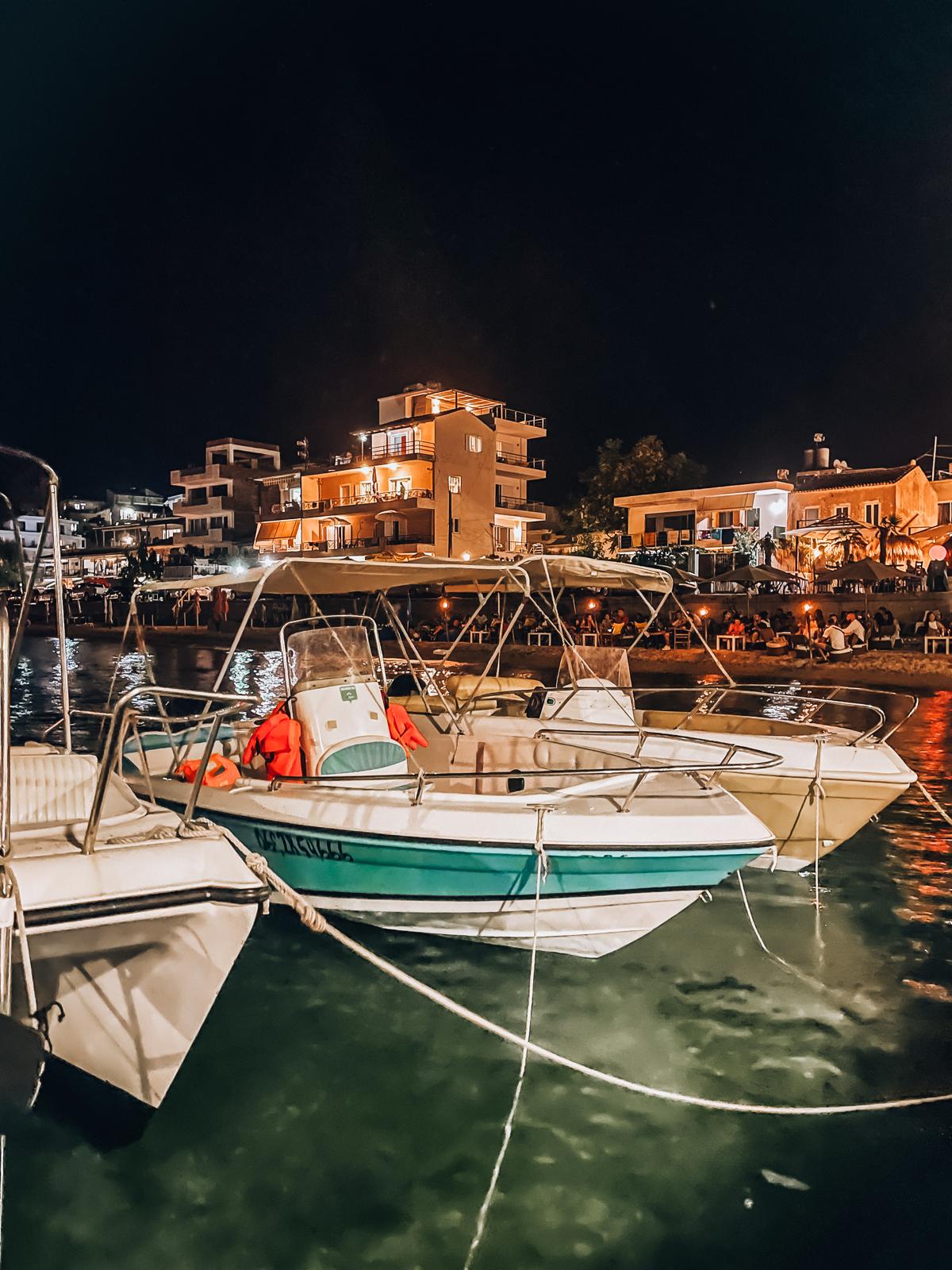 View from the harbor in Himara looking out over the town with buildings rising along the hillside and the sea stretching into the distance. The scene shows the port area where visitors arriving by car often look for parking in Himare before walking into the city center.
