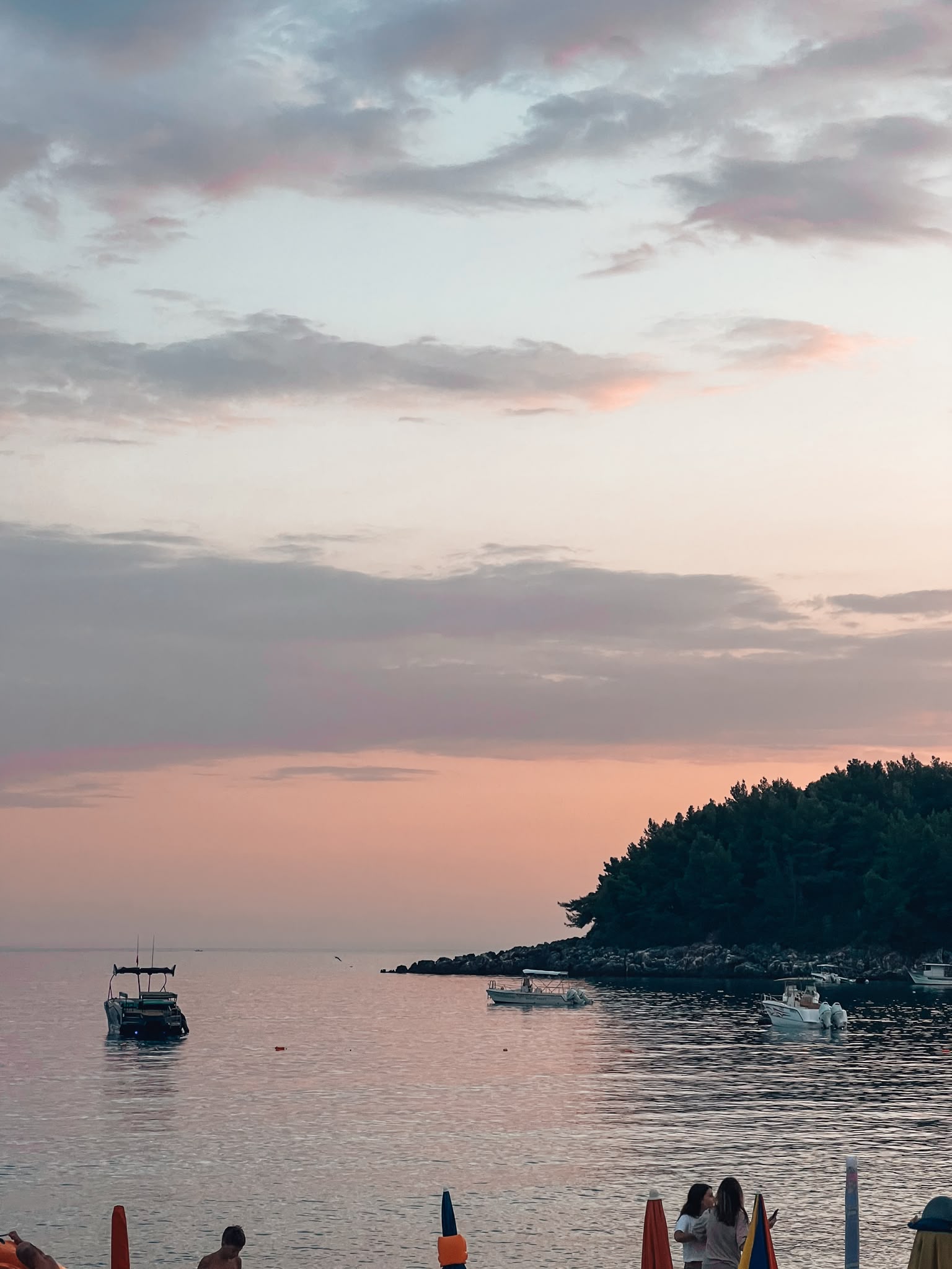 Himara Beach at sunset with golden light reflecting across the calm sea and people strolling along the shoreline. The warm evening colors and relaxed waterfront atmosphere show why it is often included among the Best Beaches in Himare.