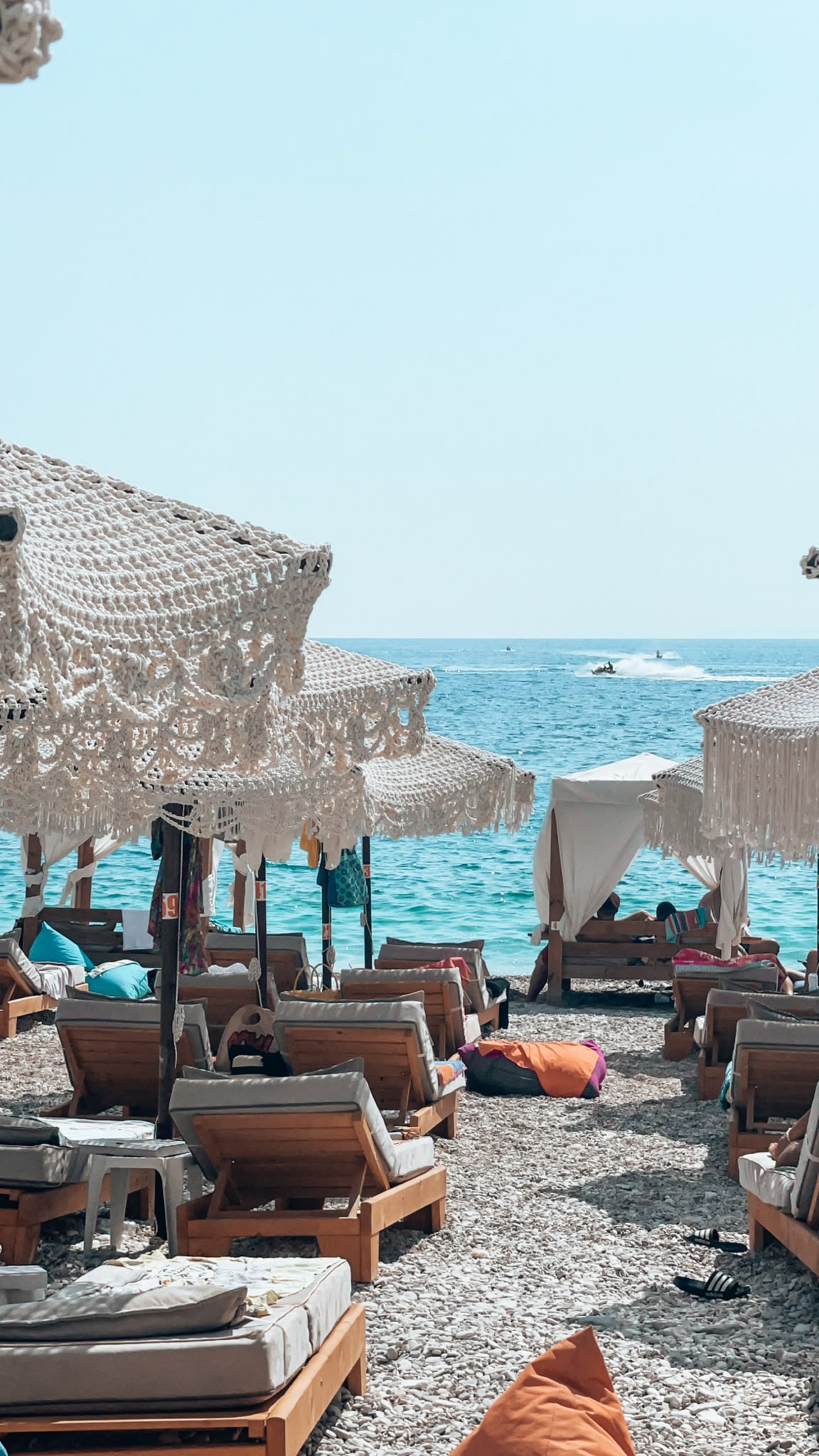 Llamani Beach with clear turquoise water gently meeting a small crescent of pebbled shore surrounded by green hills. The calm, sheltered bay highlights its place among the Best Beaches in Himare.