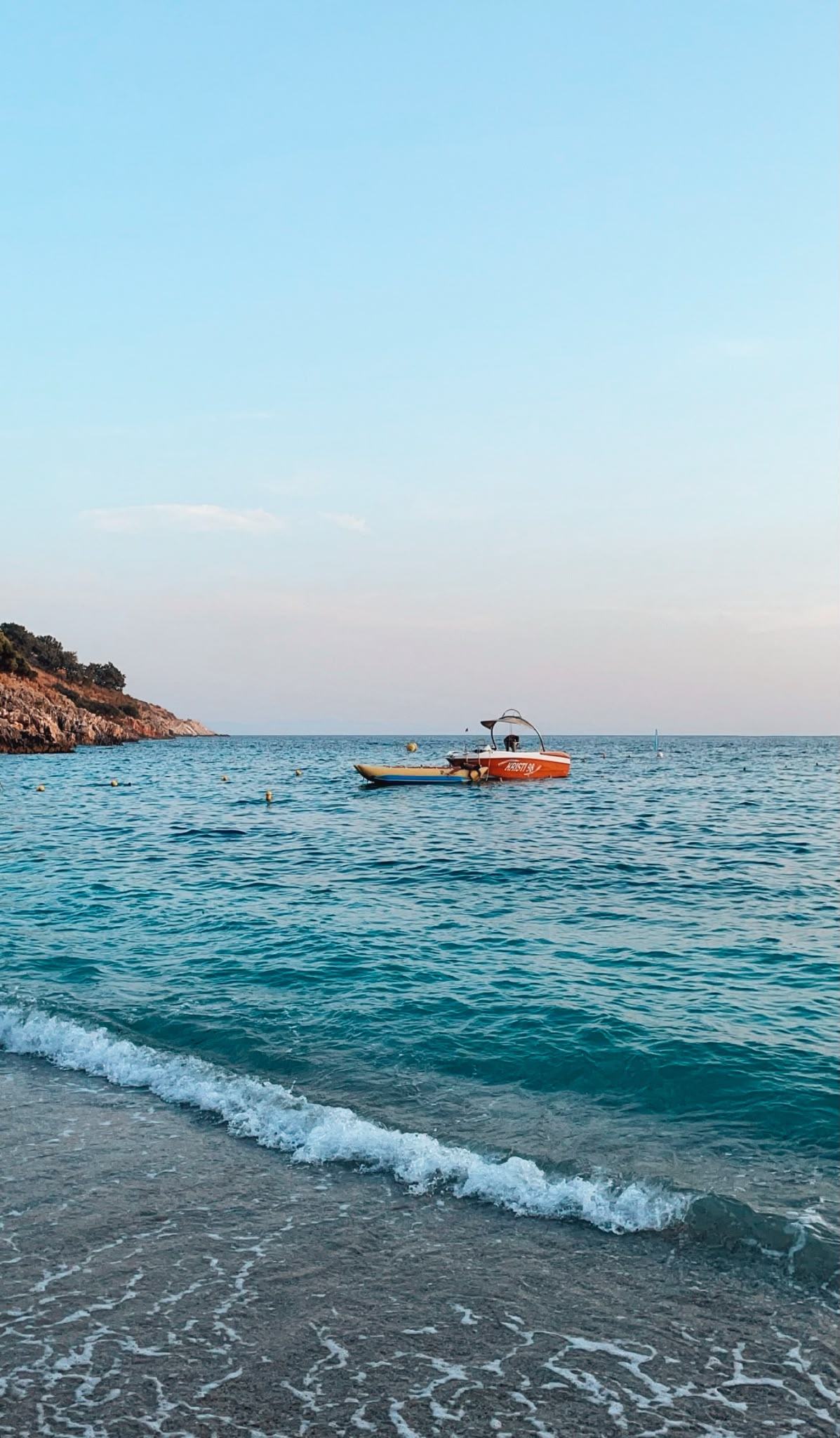 lamani Beach in Himarë framed by steep hills and a sheltered cove with clear turquoise water and a pebbled shoreline. The scenic bay is one of the beaches in Himarë reachable by scooter, known for its calm waters and dramatic natural setting along the Albanian Riviera.