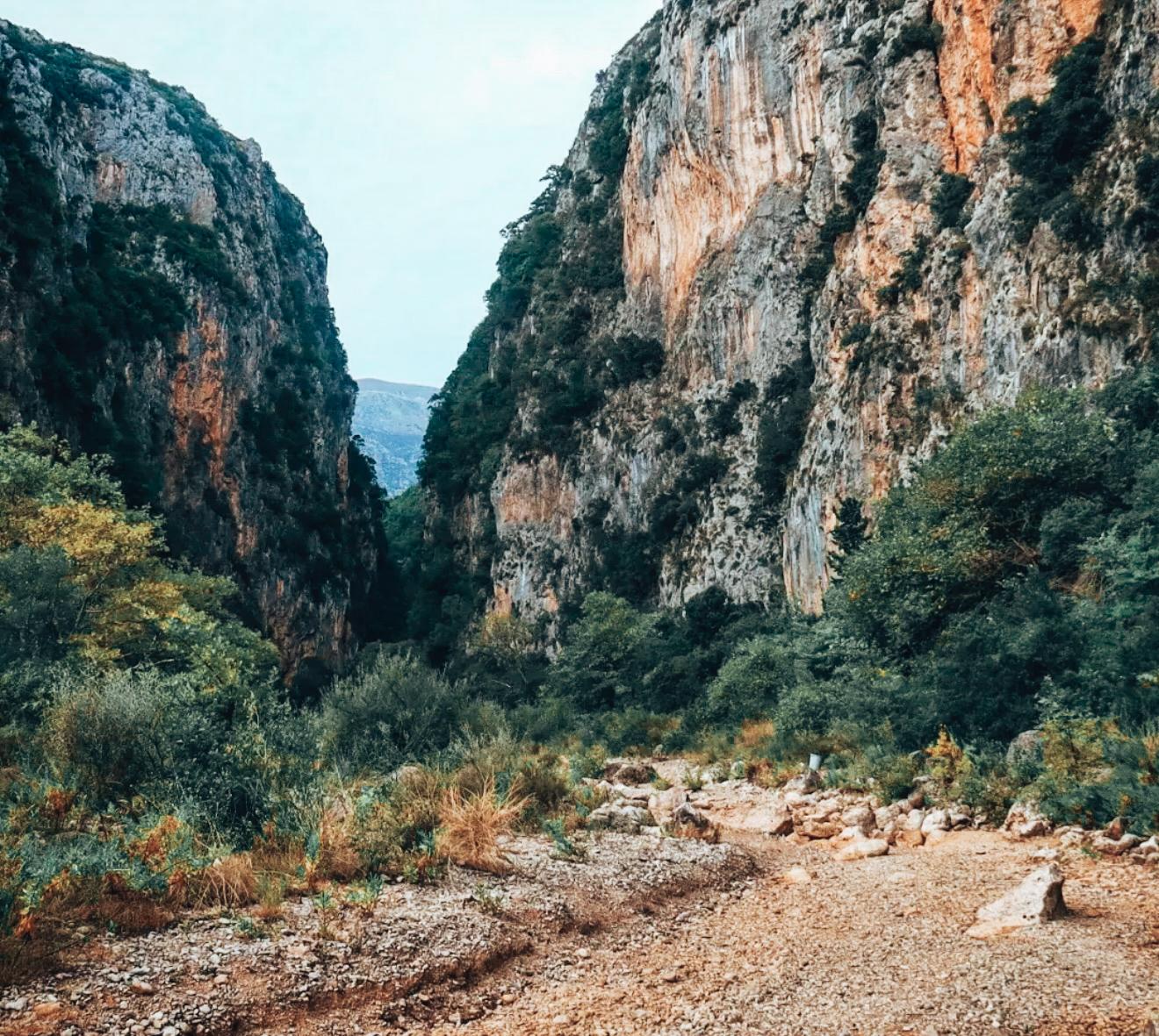 View of Gjipe Canyon and the walking road leading toward Gjipe Beach. Steep rocky cliffs rise above the canyon while the path follows the coastline, showing part of the route used to get to Gjipe Beach from Himarë.