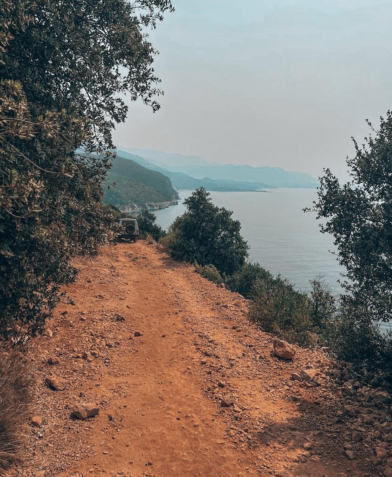 Narrow walking path leading toward Gjipe Beach through rugged coastal terrain and Mediterranean vegetation. The trail shows the final section of the journey for visitors following the route from Himarë to Gjipe Beach on foot.