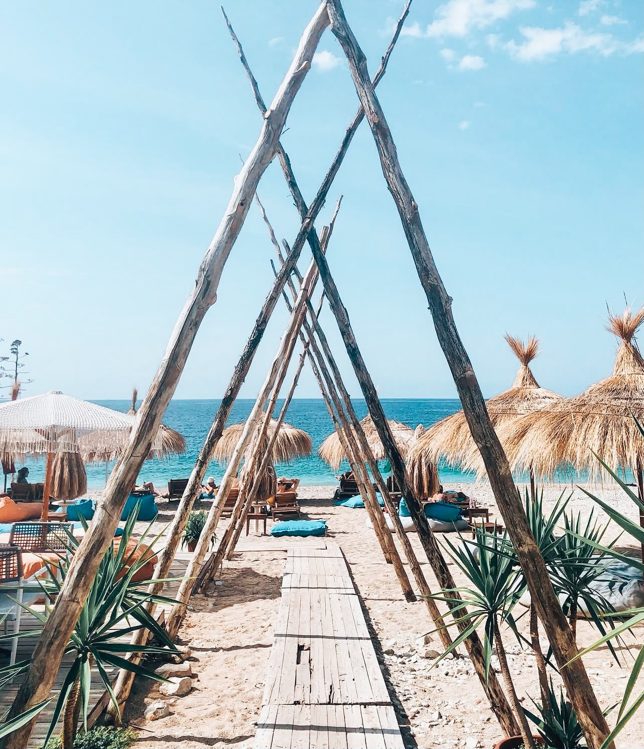 Potami Beach with a wide pebble shoreline, crystal clear blue water, and rugged mountains rising behind the coast. The spacious beach and natural surroundings make it a popular choice among the best quiet beaches near Himarë you can walk to.