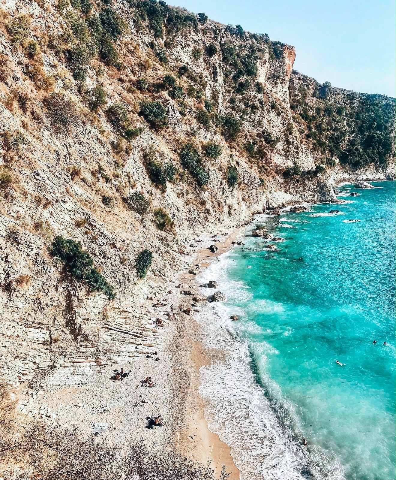 View of the Filikuri coastline with steep rocky cliffs meeting clear turquoise water along a secluded stretch of shore. The remote setting and lack of development showcase why this area is considered one of the best quiet beaches near Himarë you can walk to.