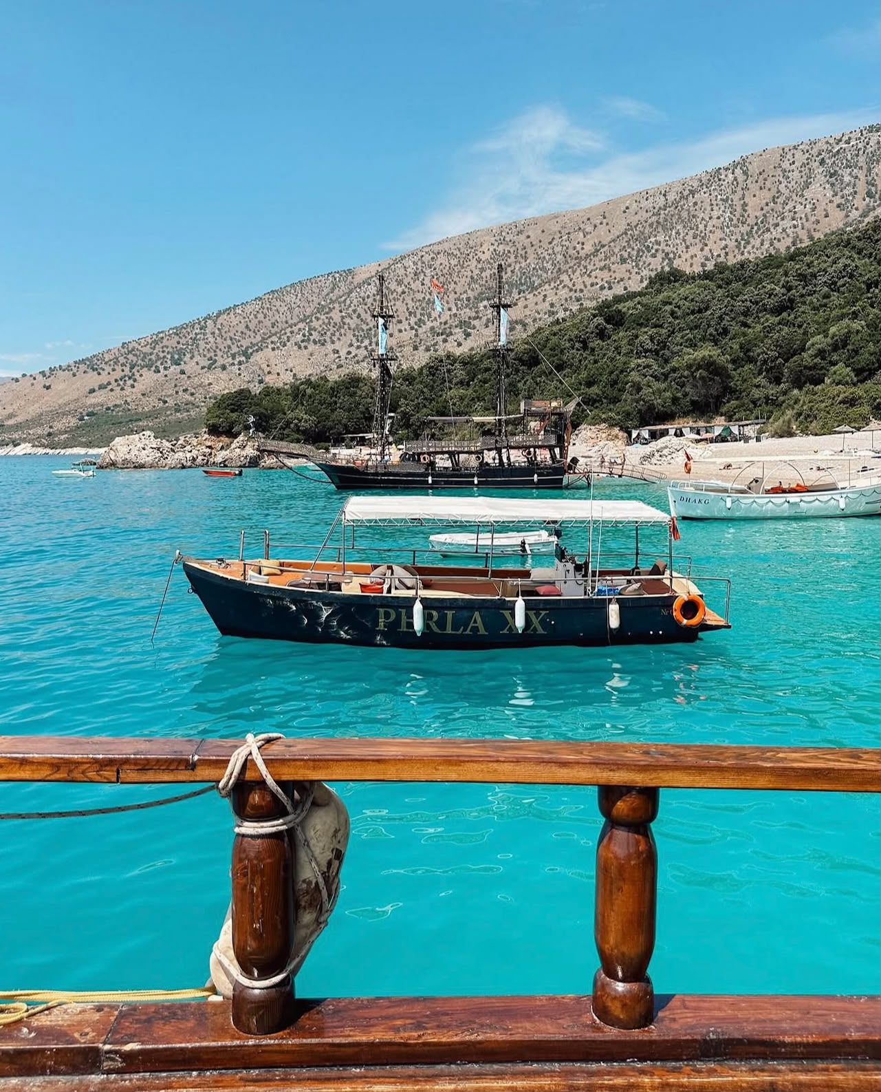Secluded Krorëza Beach with bright turquoise water and a curved sandy shoreline surrounded by green hills. The calm, clear sea meets the shore in a remote bay, emphasizing its natural, untouched setting.