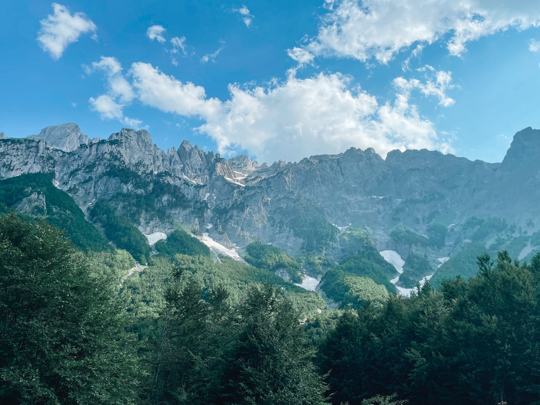 Rugged peaks of the Albanian Alps rise above green valleys, forests, and traditional mountain landscapes in northern Albania. The dramatic scenery highlights the natural beauty and adventure opportunities found throughout this remote mountain region.