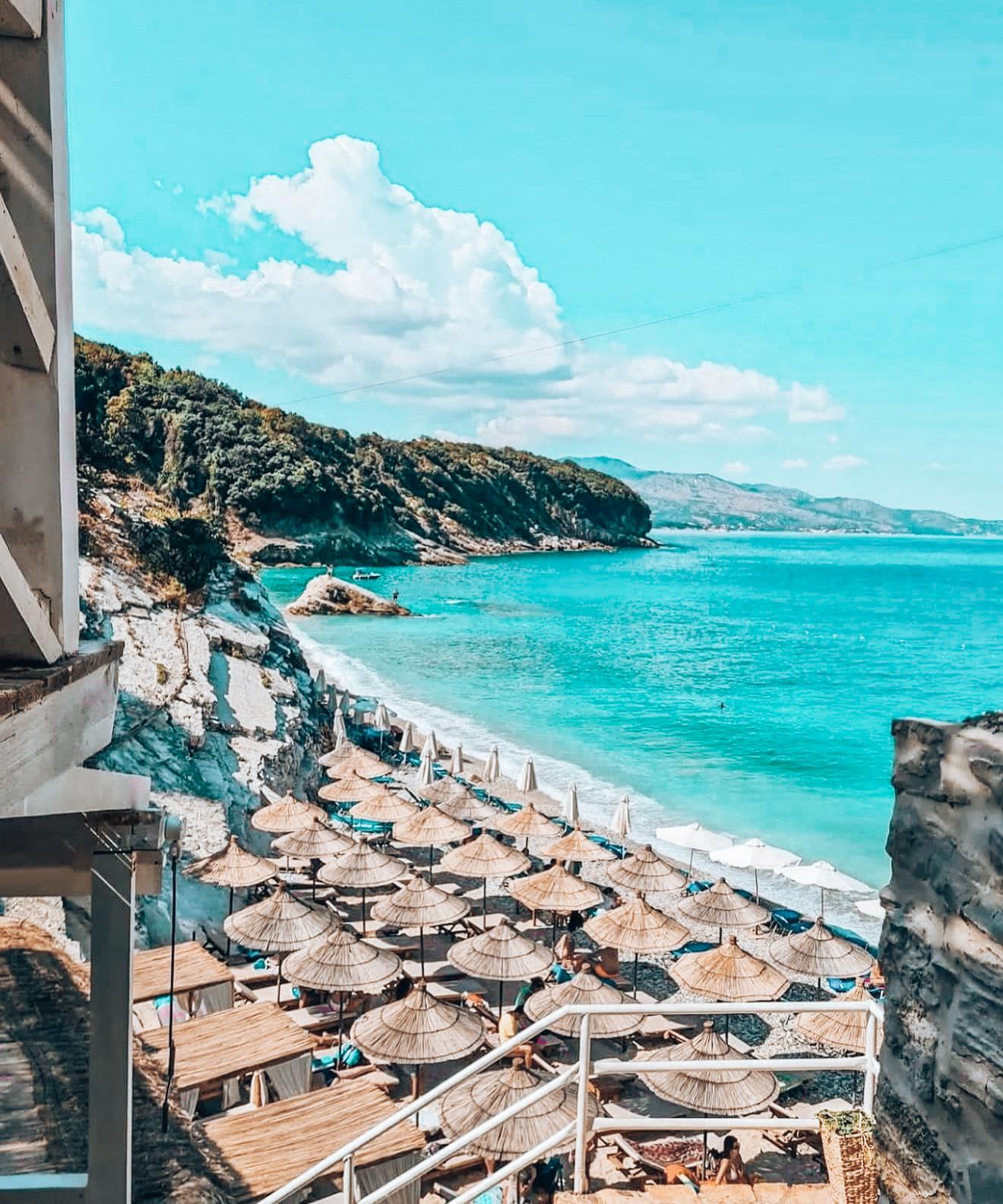 Pulebardha Beach near Ksamil with clear turquoise water, white pebbles, and beachgoers relaxing along the shoreline on a sunny day. This quieter stretch of coast is one option to consider when exploring Are There Free Beaches in Ksamil.