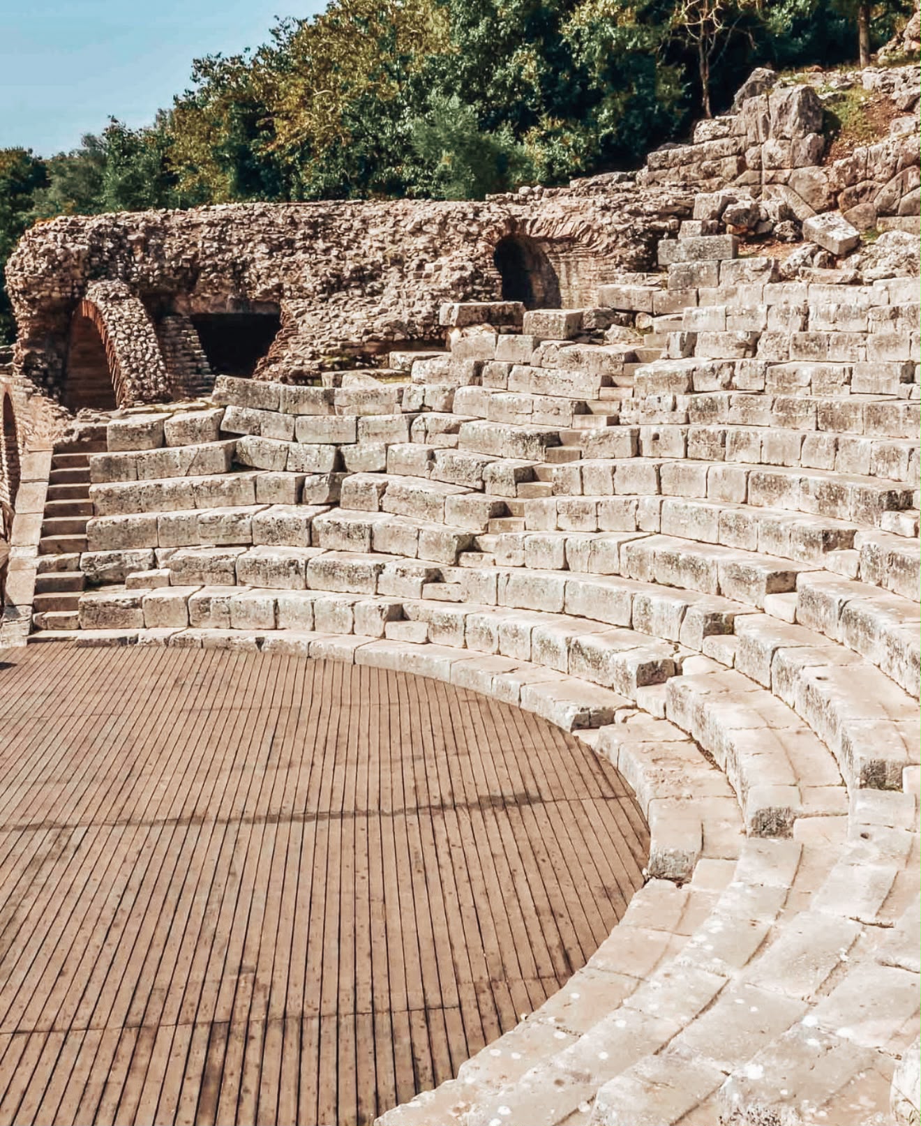 Archaeological ruins within Butrint National Park showing stone pathways and remnants of ancient buildings. The scene emphasizes the preserved historical layout and textures of aged stonework.