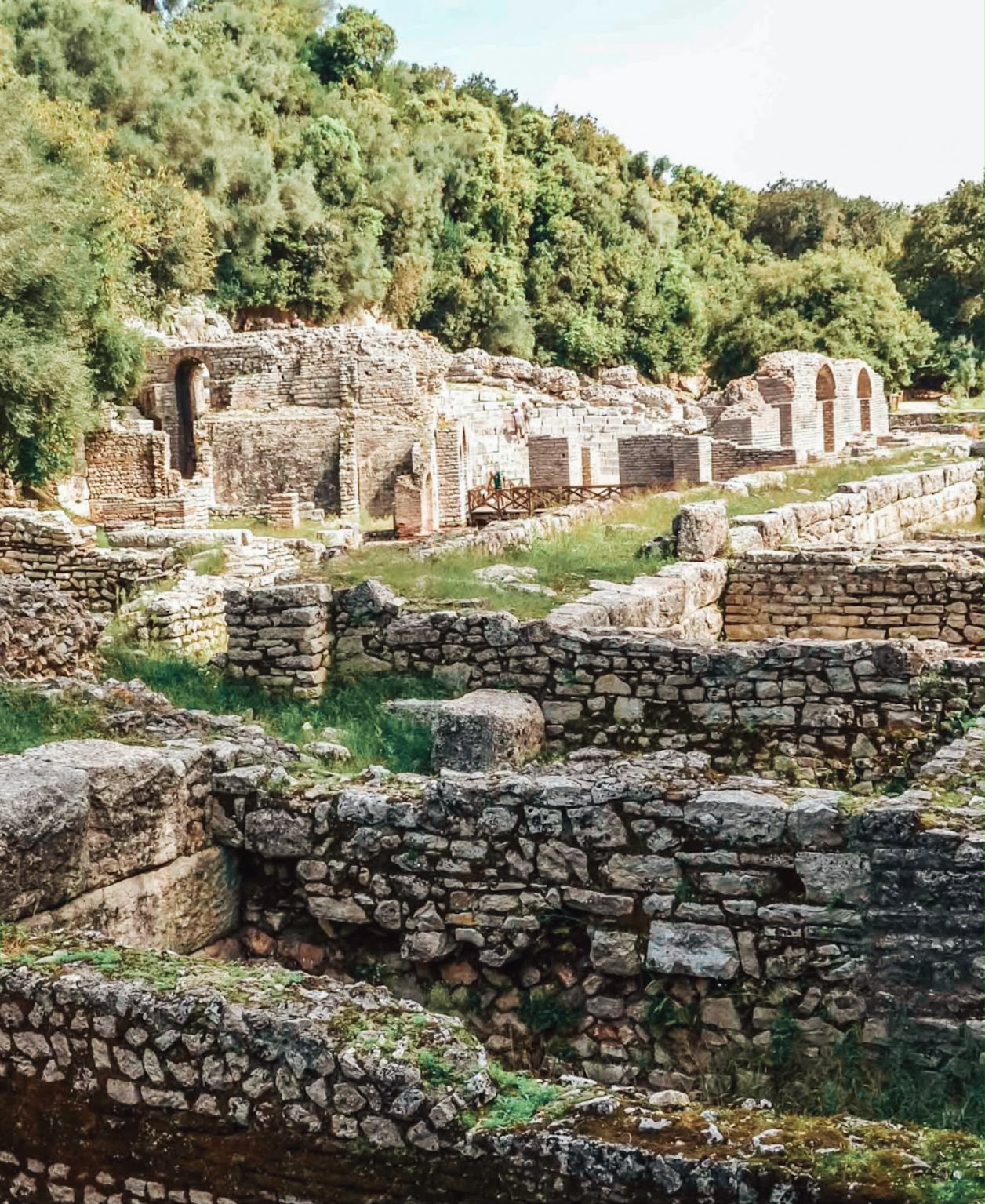 Ancient stone ruins inside Butrint National Park featuring weathered walls and archaeological remains. The structures show signs of age and history, blending into the surrounding natural setting.
