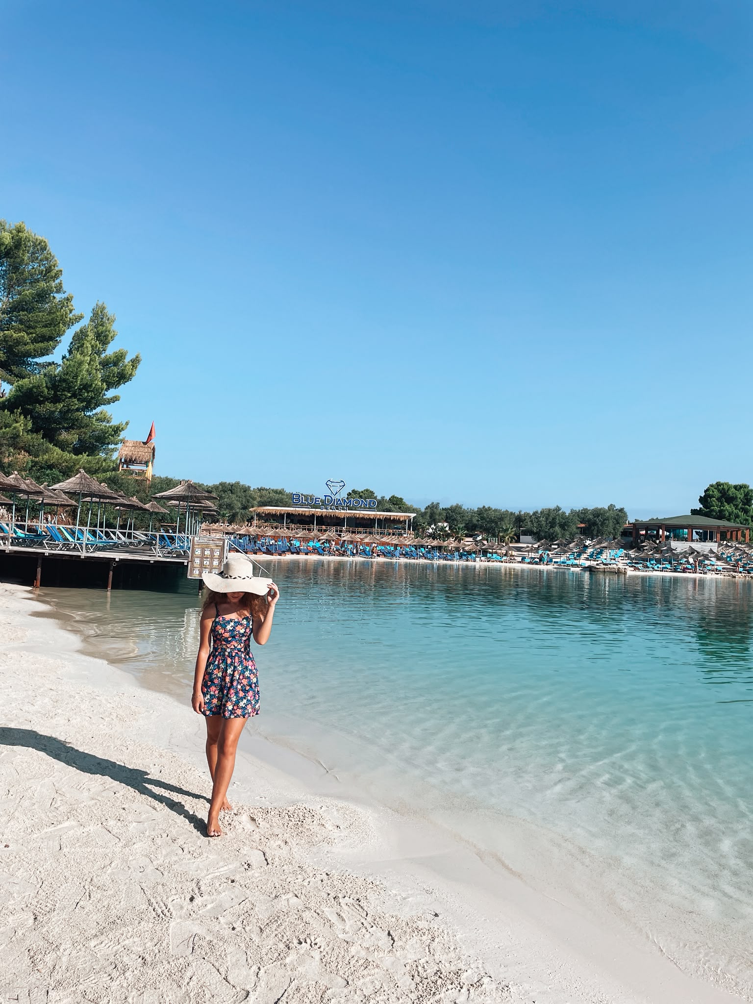A girl standing on Ksamil Beach with turquoise water and small islands in the background. The sunny coastal setting captures the relaxed atmosphere of a beach day in Ksamil.