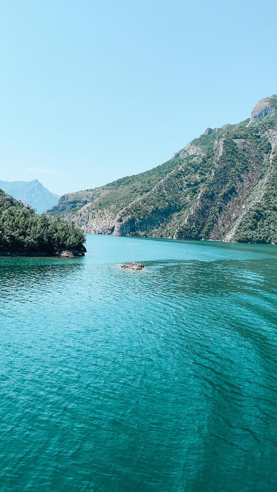 Turquoise water winds through the steep, forested mountains of Komani Lake as a ferry travels between dramatic cliffs. This scenic boat journey is the main route connecting Valbona and Theth for travelers visiting without hiking.