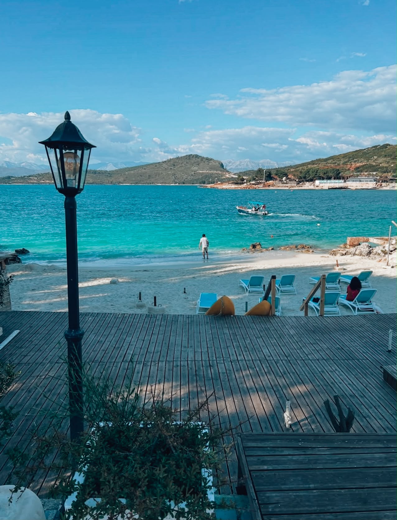 Turquoise waters and small islands of Ksamil coastline viewed from a roadside, with beaches, greenery, and seaside buildings stretching along the shore. The scenic view highlights the coastal setting travelers see when exploring where to stay in Ksamil.