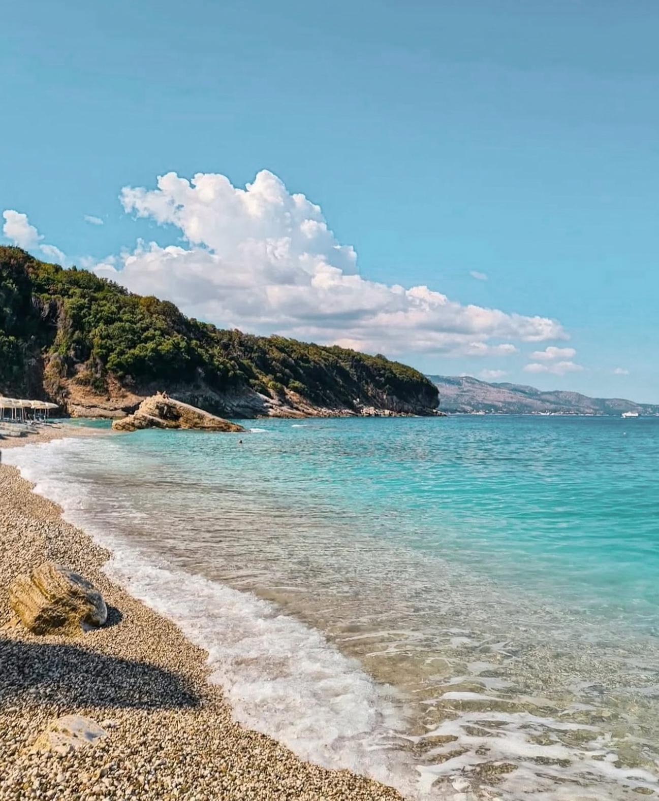 Pulbardha Beach near Ksamil with clear turquoise water, rocky shoreline, and sunbeds along the coast surrounded by Mediterranean scenery. A peaceful beach spot that helps travelers compare Ksamil vs Saranda when deciding where to stay in Albania.