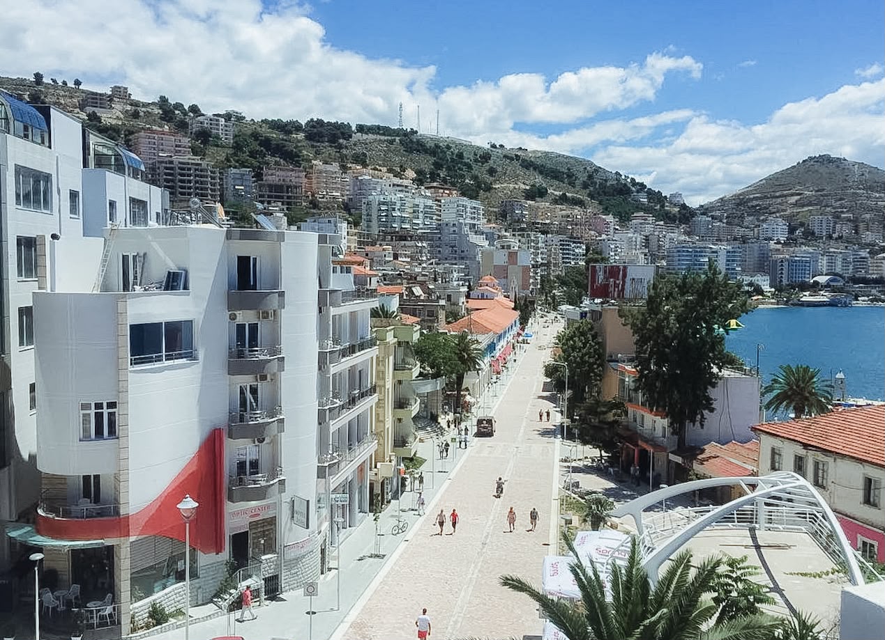 Saranda’s main boulevard lined with palm trees, shops, cafes, and busy pedestrian areas along the waterfront. The lively street scene helps travelers understand the central atmosphere when choosing where to stay in Saranda.