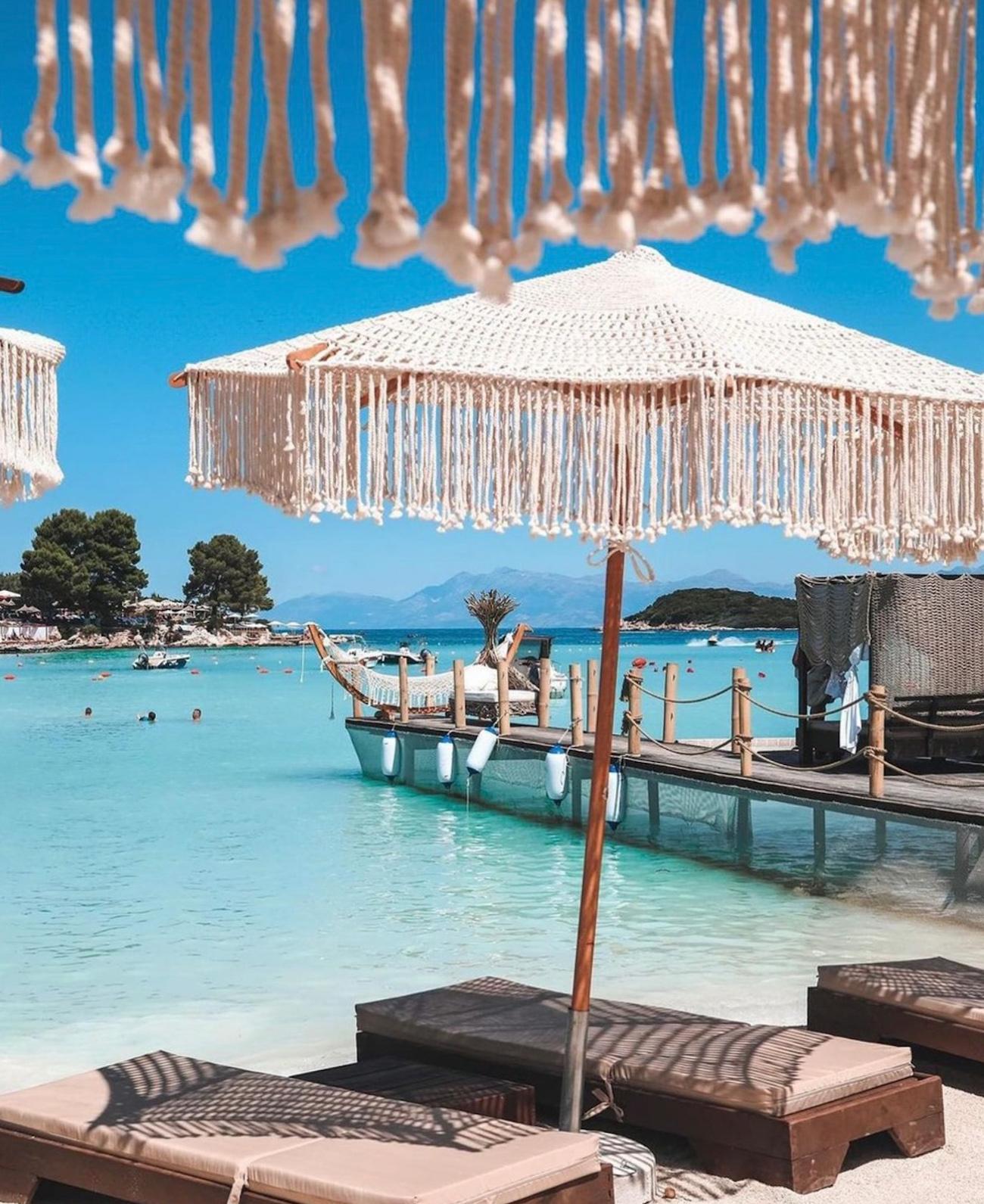Rows of white sunbeds and matching umbrellas line the shore of Ksamil Beach beside calm turquoise water. A classic beach setup for relaxing and swimming during 2 Days in Ksamil.